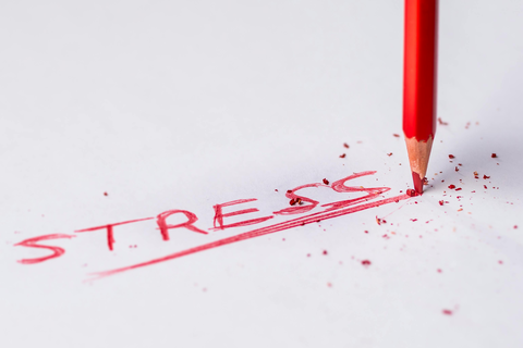 Auf einem weißen Hintergrund steht mit rotem Bleistift "Stress" geschrieben. Der Ausdruck ist unterstrichen. Am Ende des Unterstrichs ist der rote Bleistift aufgedrückt.
