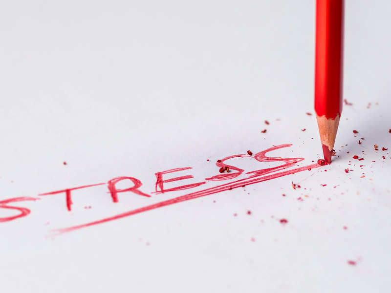 Auf einem weißen Hintergrund steht mit rotem Bleistift "Stress" geschrieben. Der Ausdruck ist unterstrichen. Am Ende des Unterstrichs ist der rote Bleistift aufgedrückt.