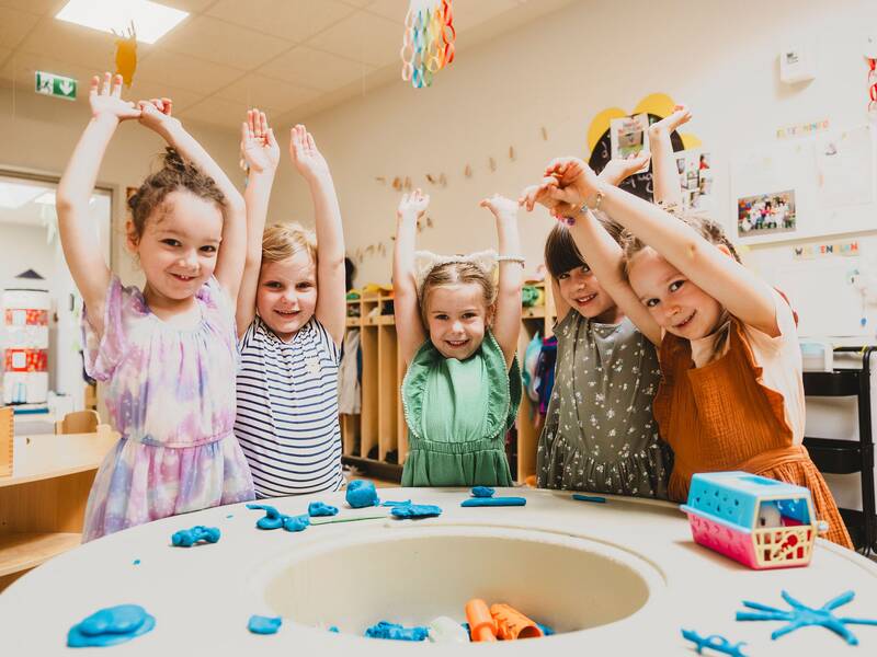 fünf Mädchen stehen lächelnd um einen Spieltisch und strecken die Arme in die Luft