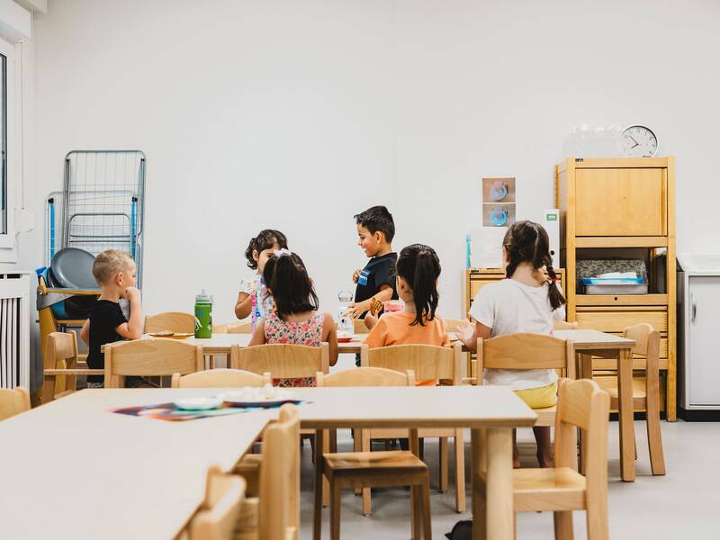 Blick in den Gruppenraum, an einem Holztisch sitzen sechs Kinder und spielen gemeinsam