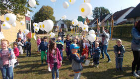 Eine große Gruppe an Kindern lässt Luftballons mit Postkarten daran in die Luft steigen