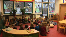 Kinder sitzen in einem Sitzkreis auf dem Boden und bekommen vorgelesen