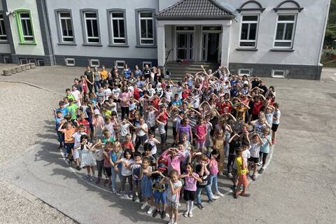 Die Schülerschaft hat sich auf dem Schulhof versammelt. Die Schüler:innen haben sich so aufgestellt, dass es aus der Vogelperspektive, wie ein Herz, aussieht.