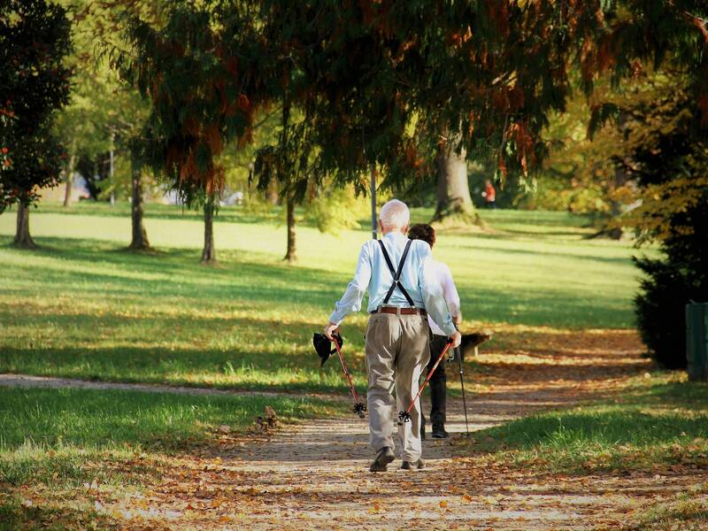 Ein älteres Paar, Mann und Frau, machen gemeinsam Nordic Walking. Die Frau geht voran und der Mann folgt ihr. Die Frau ist größtenteils verdeckt.