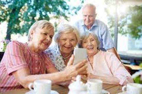 Drei ältere Frauen und ein älterer Herr an einem Kaffeetisch beschäftigen sich gemeinsam mit einem Smartphone.