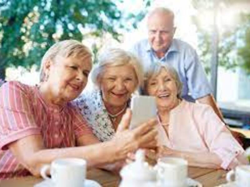 Drei ältere Frauen und ein älterer Herr an einem Kaffeetisch beschäftigen sich gemeinsam mit einem Smartphone.